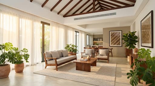 Expansive Malaysian luxury bungalow living room with high ceilings, sheer white drapes filtering golden tropical sunlight, rich teak wood furniture, lush indoor monstera plants, and a seamless minimalist concealed ceiling ducted air conditioning slot integrated elegantly into the architectural bulkhead
